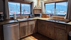 A kitchen with wooden cabinets, a refrigerator, a sink, and a window with a view of snow-covered trees.