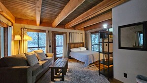 A cozy cabin interior with a wooden ceiling, a sofa, a bed, and a table.