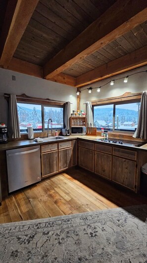 A kitchen with wooden cabinets, a refrigerator, a sink, and a window with a view of snow-covered trees. - Lookout Tower: Sleeps 4- Water Views- Near Glacier (Coram)