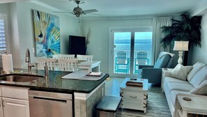 A modern kitchen with a central island, a dining area with white chairs, a living room with a sofa and a view of the ocean through large windows. - Beachfront Penthouse Located On The 9th Floor with Two Balconies & Low Host Fee (Gulf Shores)