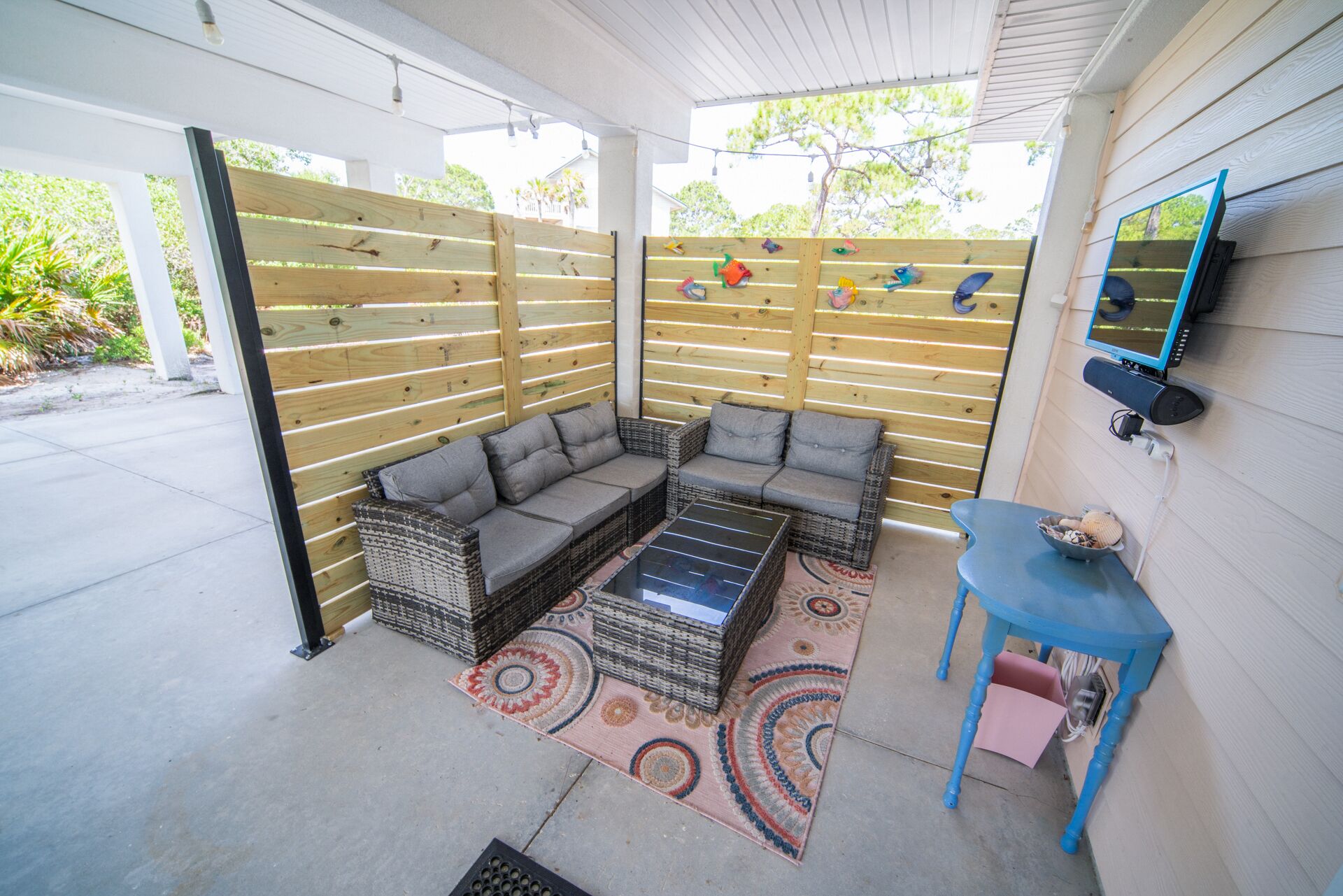 An outdoor patio with a cushioned seating area, a small table, and a decorative rug.