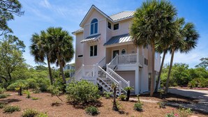 A two-story house with a balcony, surrounded by palm trees and a landscaped garden. - Secluded 4BR/3.5BA, inside St. George Plantation (St. George Island)