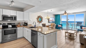 A modern kitchen with a central island, stainless steel appliances, and a view to the outside. - On the Beach, Panoramic Ocean View, Renovated Pelican Beach Condo (Destin)