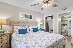 A bedroom with a tufted headboard, star-patterned bedding, two bedside lamps, a ceiling fan, and a framed artwork on the wall. - On the Beach, Panoramic Ocean View, Renovated Pelican Beach Condo (Destin)