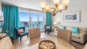A room with a large window, a chandelier, wicker furniture, and a view of the ocean. - On the Beach, Panoramic Ocean View, Renovated Pelican Beach Condo (Destin)