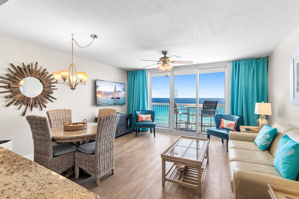 A spacious living area with a dining table, wicker chairs, a sofa, and a ceiling fan. - On the Beach, Panoramic Ocean View, Renovated Pelican Beach Condo (Destin)