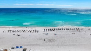 A beach with rows of umbrellas and sun loungers, a clear blue sky, and the ocean. - On the Beach, Panoramic Ocean View, Renovated Pelican Beach Condo (Destin)