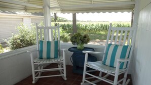 Two white rocking chairs with teal cushions, a small round table with a woven top, and a vase of flowers.