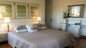 A neatly arranged bedroom with a large bed, two bedside lamps, a mirror, and framed artwork on the wall.