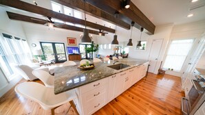 A spacious kitchen with a large island, wooden flooring, pendant lighting, and a view of the outdoors. - Bayfront, Handicap-Friendly, Pool & Elevator, Kayaks (St. George Island)