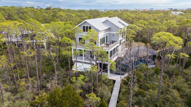 A two-story house with a large deck and a glass conservatory, surrounded by dense forest. - Bayfront, Handicap-Friendly, Pool & Elevator, Kayaks (St. George Island)