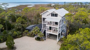 A multi-story house with a balcony on the second floor, surrounded by trees and a view of the beach. - Bayfront, Handicap-Friendly, Pool & Elevator, Kayaks (St. George Island)
