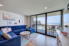 A modern living room with a blue sofa, a round coffee table, and a view of the ocean through large windows.