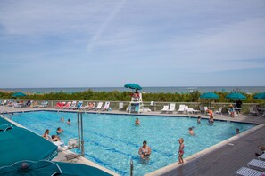 A swimming pool with lounge chairs and umbrellas, surrounded by a wooden deck and a view of the ocean.
