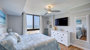 Un dormitorio con cama, cómoda, televisor y un espejo grande.