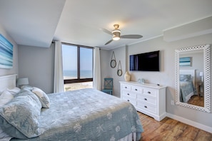 A bedroom with a bed, dresser, TV, and a large mirror.