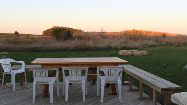 Una terraza al aire libre con una mesa de madera y sillas de plástico blanco.