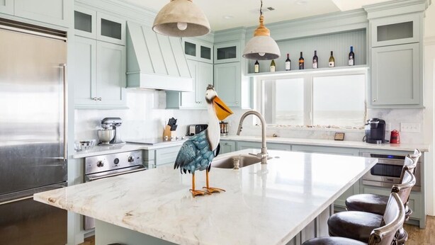 A modern kitchen with light blue cabinets, a marble island, stainless steel appliances, and a decorative bird sculpture. - Bach Haus: 4  BR, 3  BA House in Gilchrist, Sleeps 18 (Bolivar Peninsula)