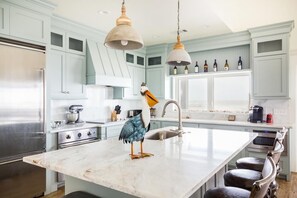 A modern kitchen with light blue cabinets, a marble island, stainless steel appliances, and a decorative bird sculpture.