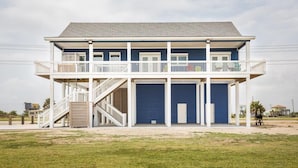 A two-story building with a balcony, a staircase, and a garage door. - Bach Haus: 4  BR, 3  BA House in Gilchrist, Sleeps 18 (Bolivar Peninsula)