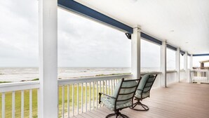 A covered porch with two chairs facing the ocean, white railings, and a view of the beach. - Bach Haus: 4  BR, 3  BA House in Gilchrist, Sleeps 18 (Bolivar Peninsula)
