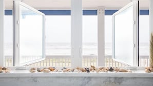 A room with a large window overlooking the beach, a marble bench with seashells, and a view of the ocean. - Bach Haus: 4  BR, 3  BA House in Gilchrist, Sleeps 18 (Bolivar Peninsula)