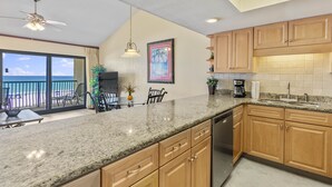 A kitchen with granite countertops, wooden cabinets, a ceiling fan, and a large window overlooking a balcony.