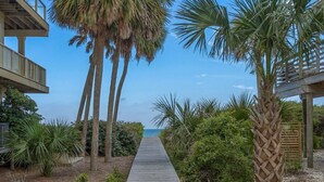 A wooden pathway leading to a beach, flanked by palm trees and a wooden structure. - 3BR/2BA 1st Tier, Timeless Beauty w/ Easy Beach Access & Clubhouse w/ Pool! (St. George Island)