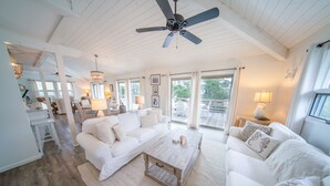A spacious living area with white furniture, a ceiling fan, and large windows offering views of the outdoors. - 3BR/2BA 1st Tier, Timeless Beauty w/ Easy Beach Access & Clubhouse w/ Pool! (St. George Island)