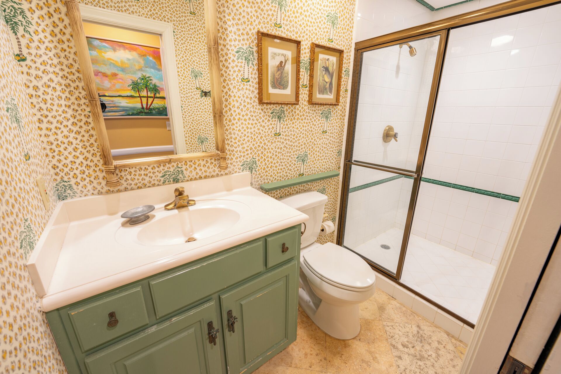 Een badkamer met een wit wastafelmeubel, groene kastjes, een toilet en een douche met glazen wanden.