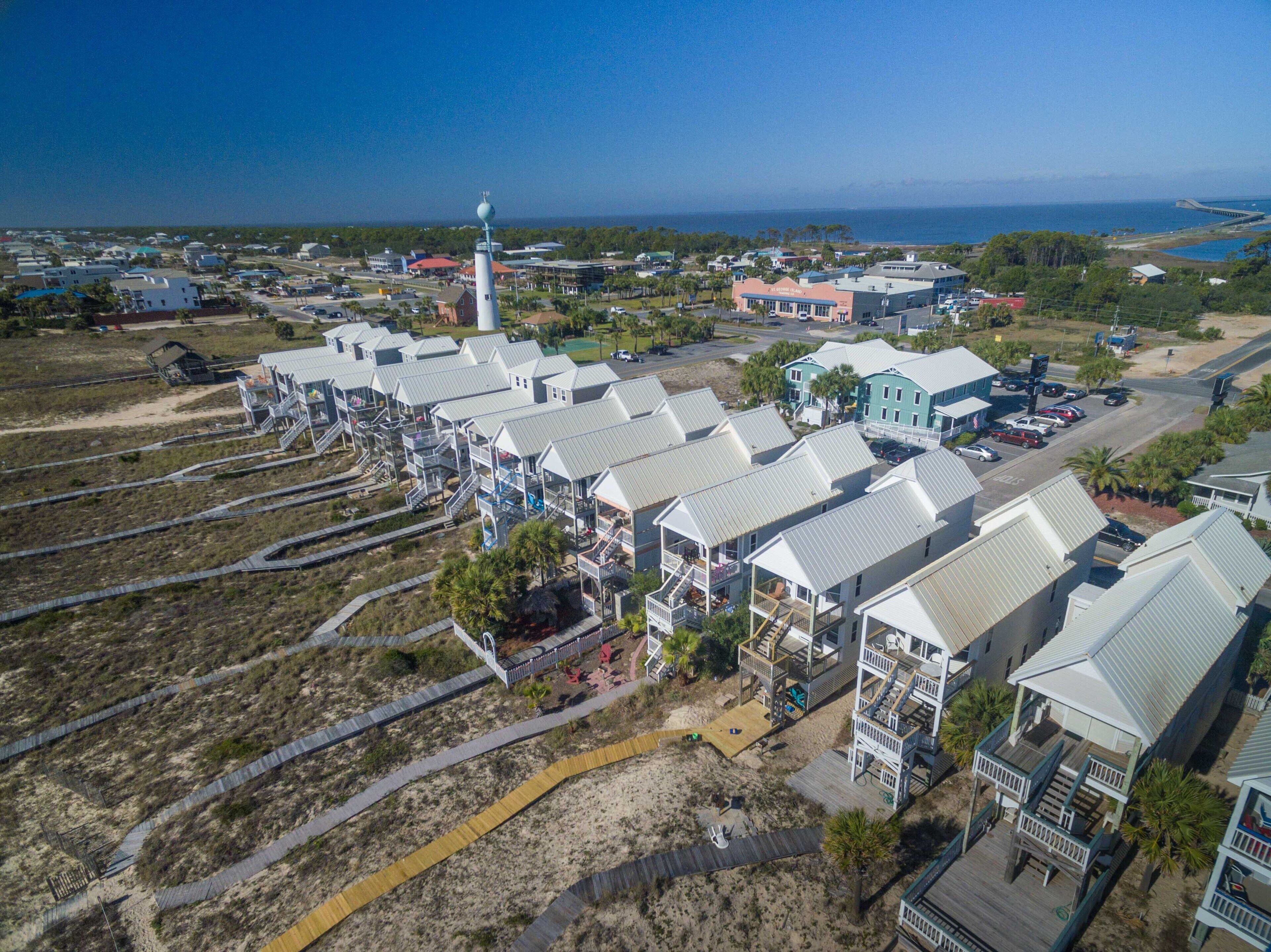 A coastal resort with multiple-story buildings, a lighthouse, and a beach access walkway.