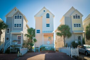 A row of three-story buildings with a central tower, a welcoming sign, and a white picket fence. - Pet Friendly, 3BR/3BA, Easy Walking Distance to Shops (St. George Island)