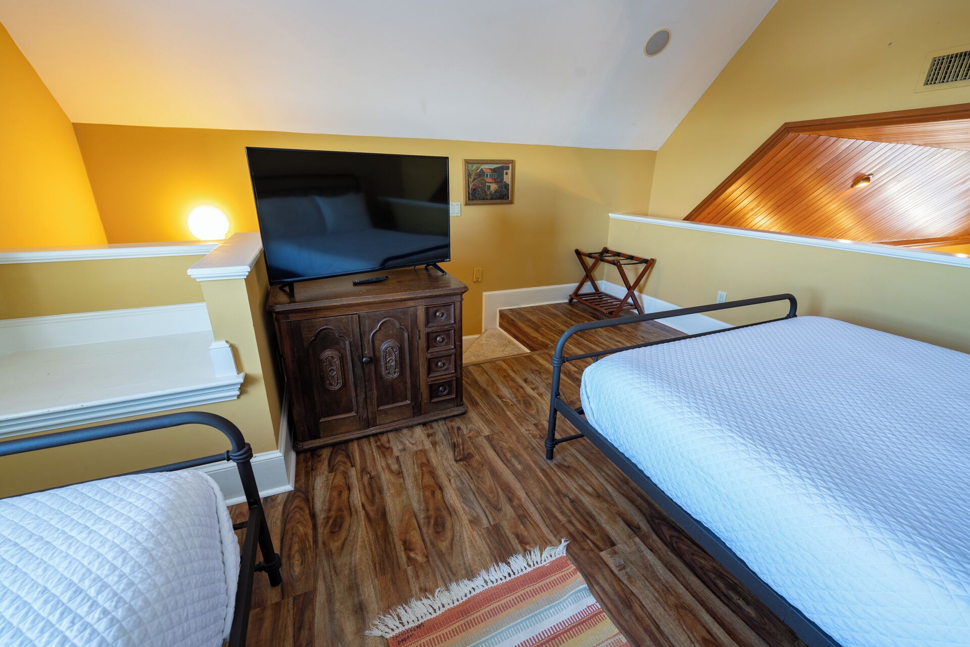Une chambre à coucher avec un lit, un téléviseur posé sur une commode en bois, une petite table et une chaise.