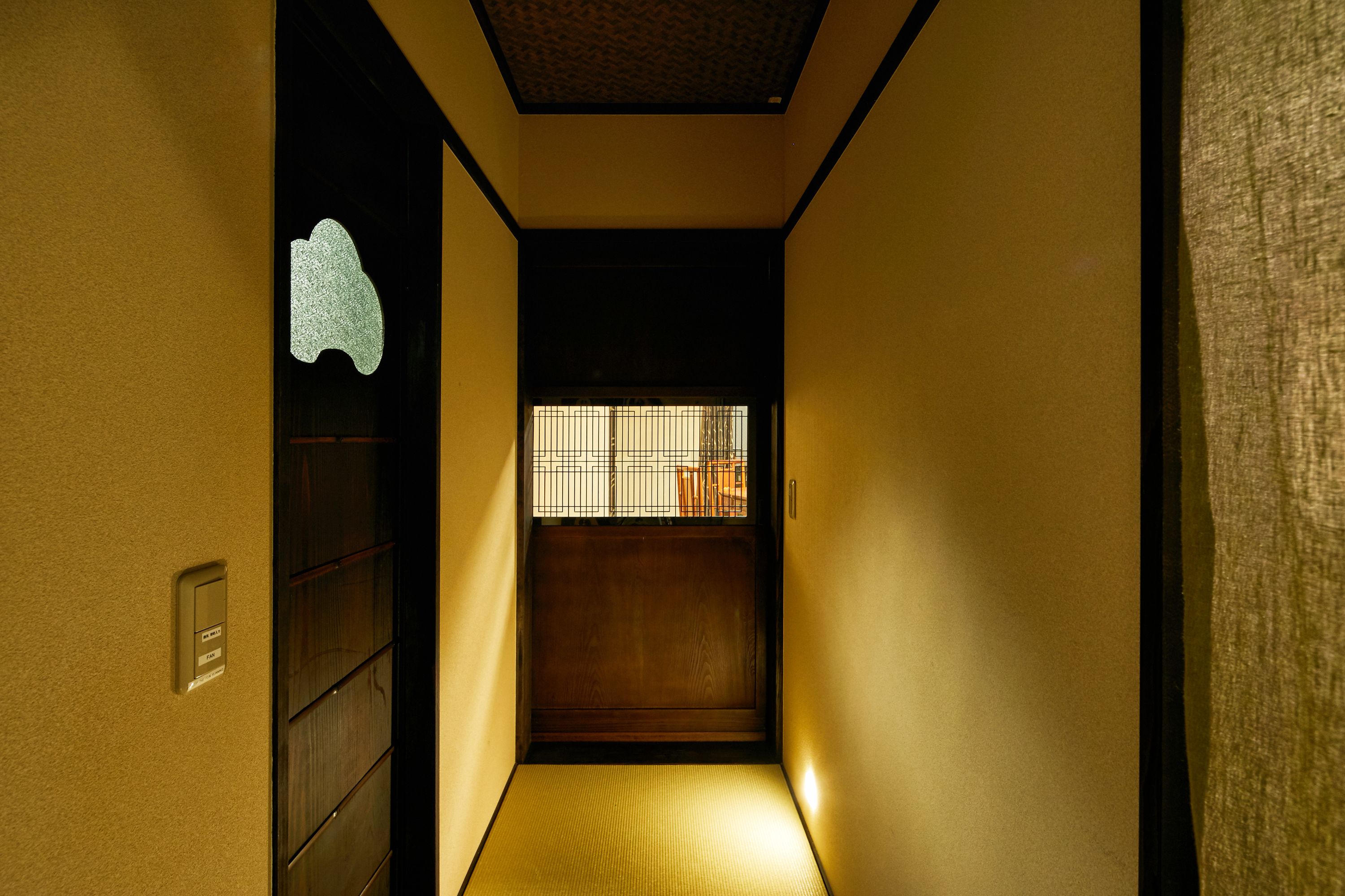 A narrow hallway with a wooden floor, a sliding door at the end, and a small window with bars.