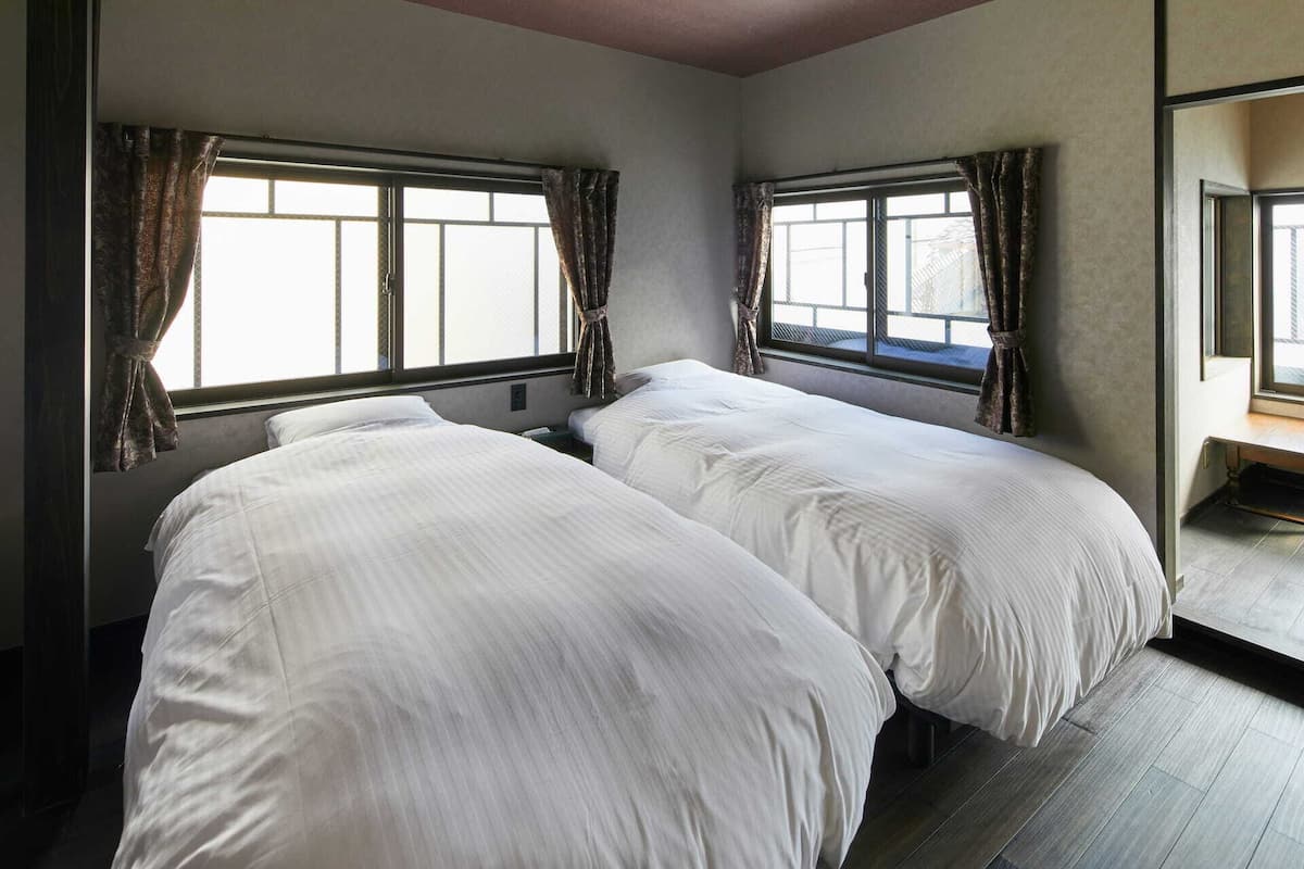 Ein Zimmer mit zwei Betten, großen Fenstern mit Vorhängen, einer Bank und einem Spiegel.