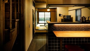 A traditional Japanese-style room with tatami flooring, a low wooden table, and a sliding door leading to a futon bed. - Eigetsu (Kyoto)