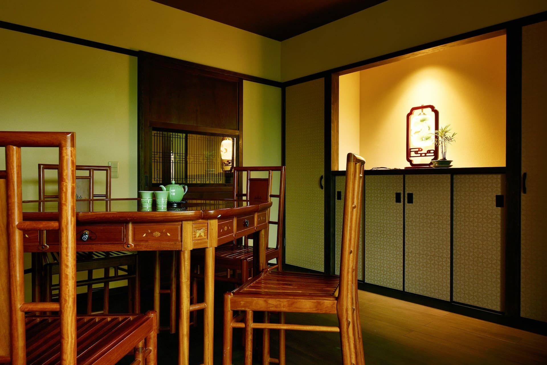A traditional Japanese-style room with tatami flooring, a low table with chairs, and a sliding door with a decorative light fixture.