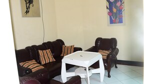 A living room with a dark brown leather sofa, a white coffee table, and a dark brown leather armchair. There are striped pillows on the sofa and a painting of flowers on the wall. - Ria Hotel Jember (Jember)