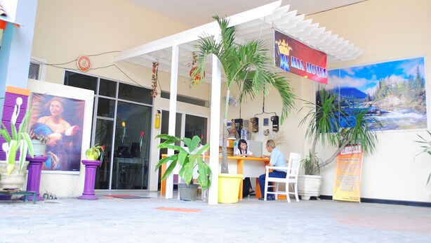 A hotel entrance with a reception desk, two guests seated, and a large poster of a person on the wall. - Ria Hotel Jember (Jember)