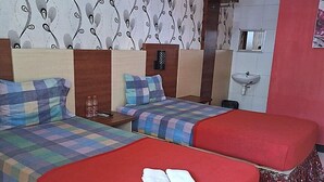 A hotel room with two beds, a small bedside table with a bottle, a wall-mounted nightstand, a mirror, and a bathroom with a sink. - Ria Hotel Jember (Jember)