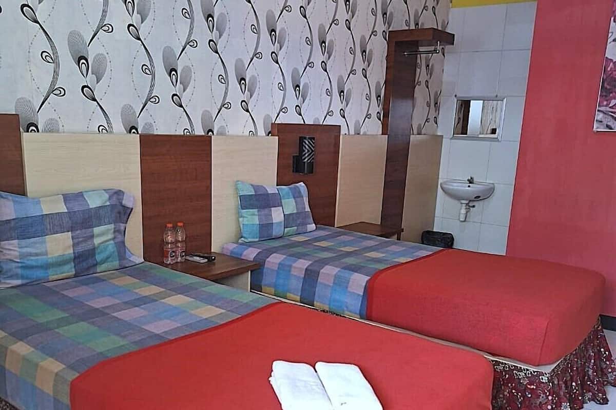 A hotel room with two beds, a small bedside table with a bottle, a wall-mounted nightstand, a mirror, and a bathroom with a sink.