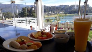 Une table avec des fruits, un verre de jus d’orange et une vue sur un lac et des montagnes.