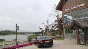 Une voiture est garée devant l’hôtel Royal Lake, d’où l’on a une vue sur un lac et des collines en arrière-plan.