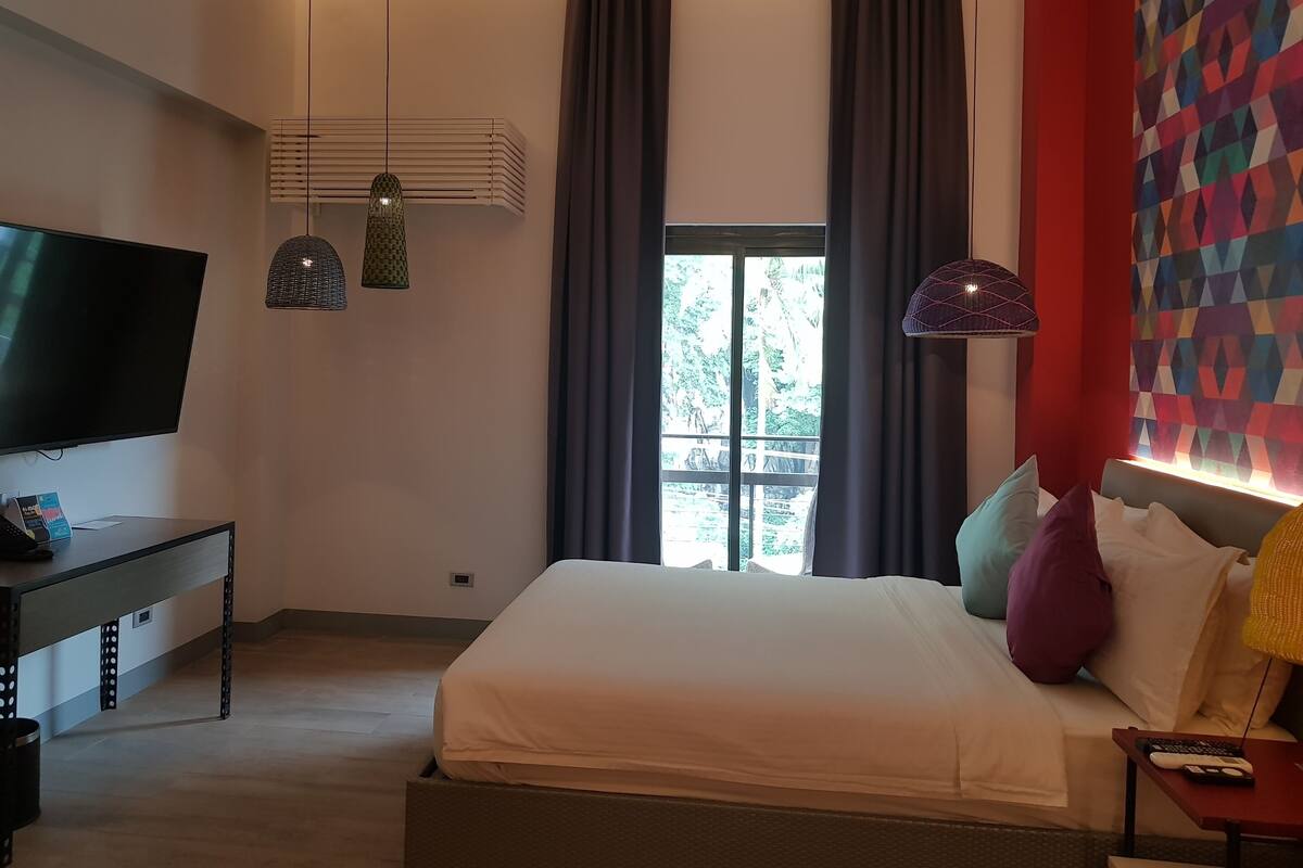 A modern bedroom with a large bed, a flat-screen TV, and a desk with a lamp.