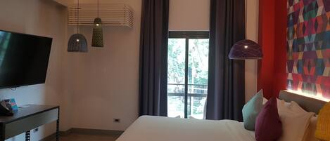 A modern bedroom with a large bed, a flat-screen TV, and a desk with a lamp.