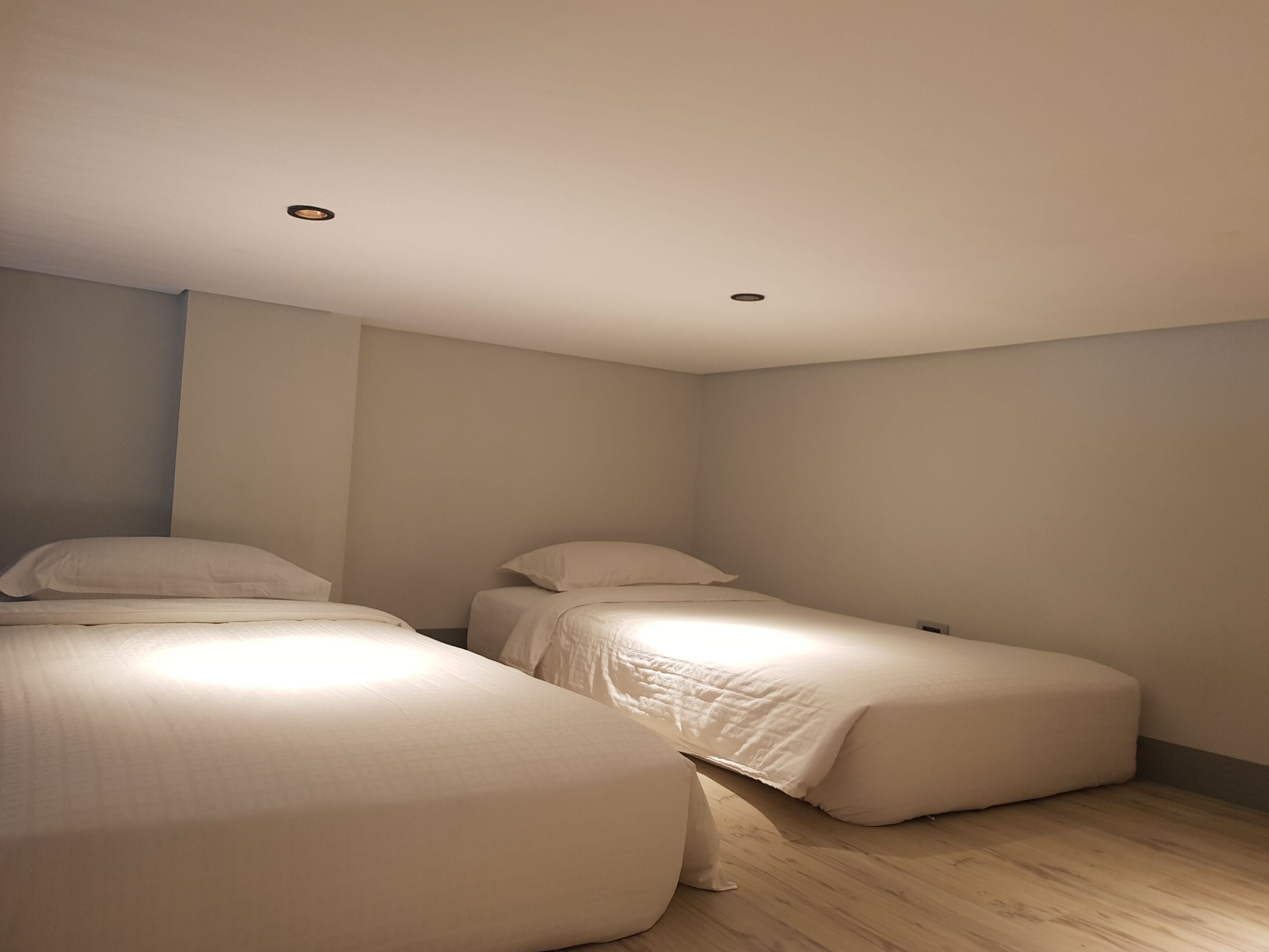 Camera da letto con due letti singoli, pavimento in legno e faretti a soffitto.