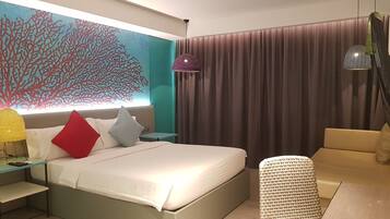 A modern hotel room with a large bed, a small side table, a sofa, a decorative wall, and a ceiling fan.