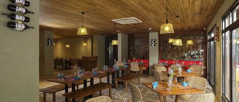 Un restaurant avec des tables et des bancs en bois, des chaises suspendues en osier et des luminaires suspendus.