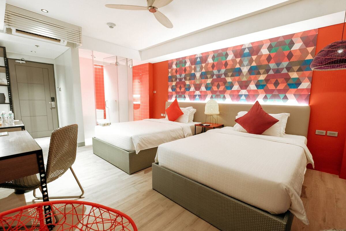 A hotel room with two beds, a dining area, and a bathroom.