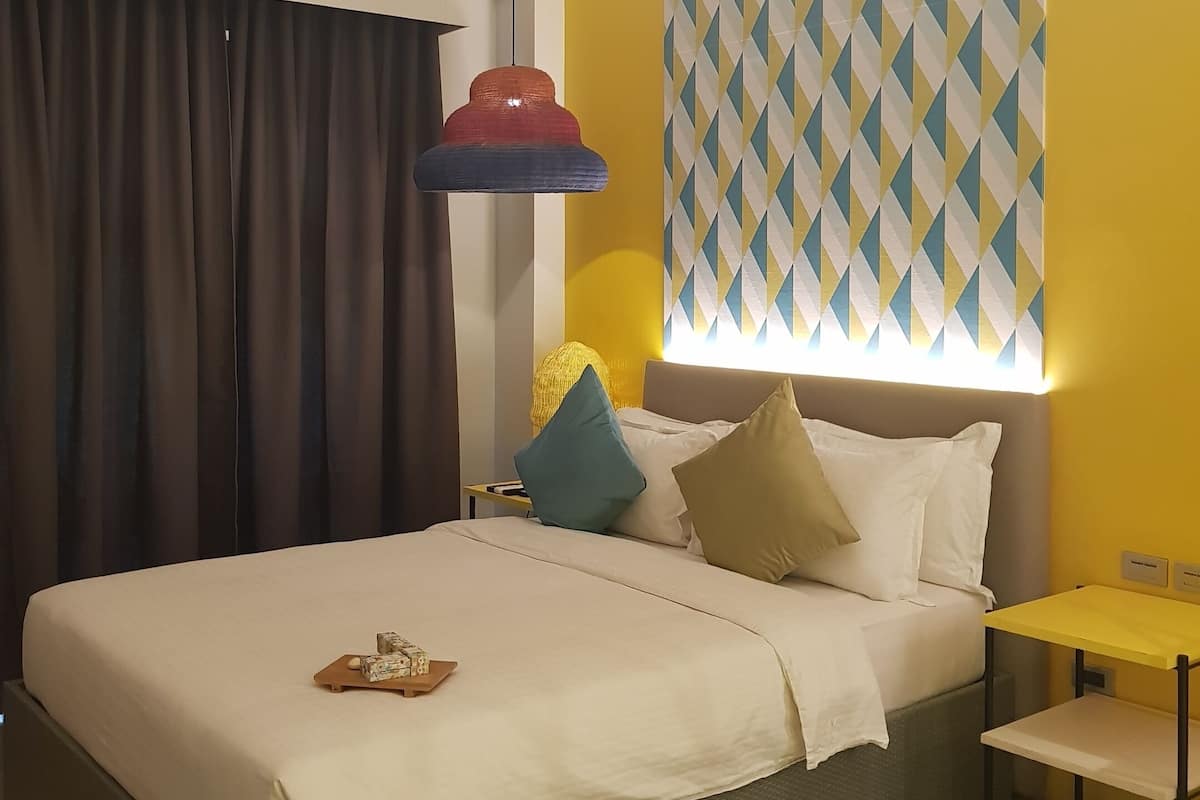 A hotel room with a bed, a bedside table, a lamp, and a patterned wall.